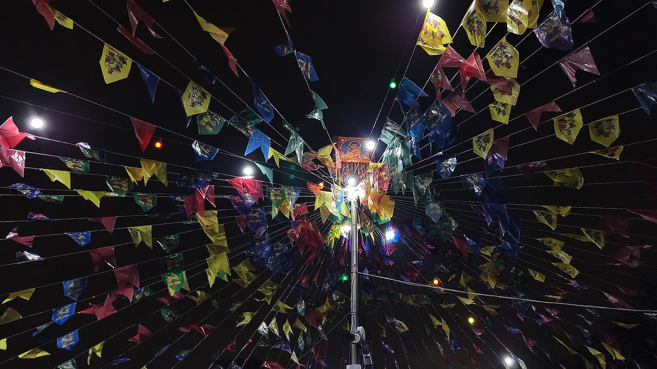 Feira de rua animada em bairro histórico com bandeirolas coloridas e músico tocando violão