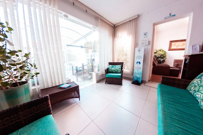 Varanda interna da Bem Me Care Residencial Sênior com poltronas turquesa, plantas e luz natural